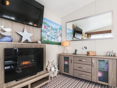 A room with a wall-mounted television above an electric fireplace a wooden cabinet with drawers and decor items a large mirror and a painting on the wall at The Rodley Pines in Cayton