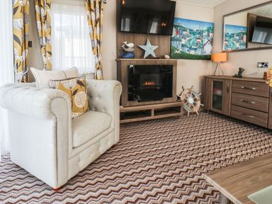 A living room with an armchair a fireplace a mounted tv a cabinet and decorative items at The Rodley Pines in Cayton