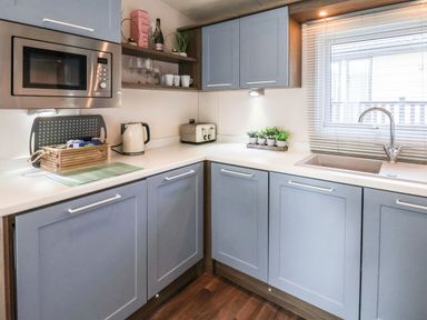 A kitchen with blue cabinets a microwave kettle toaster and a sink with a window at The Rodley Pines in Cayton