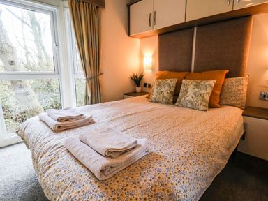 A bedroom with a bed cushions bedside tables and folded towels near a window at The Rodley Pines in Cayton