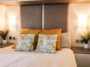 A bed with multiple pillows and bedside tables with plants and wall lamps at The Rodley Pines in Cayton