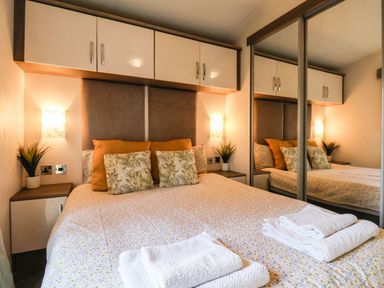 A bedroom with a bed linens, pillows, overhead cupboards, bedside tables, plants, and mirrored wardrobe doors at The Rodley Pines in Cayton