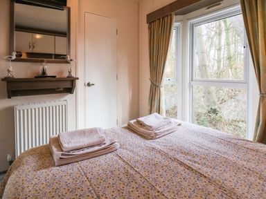 A bedroom with a bed covered in floral sheets and folded towels with a window showing trees at The Rodley Pines in Cayton