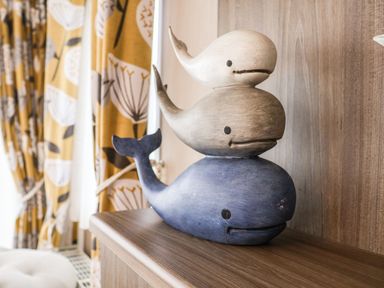 Three wooden whale figurines stacked on a wooden surface next to patterned curtains at The Rodley Pines in Cayton