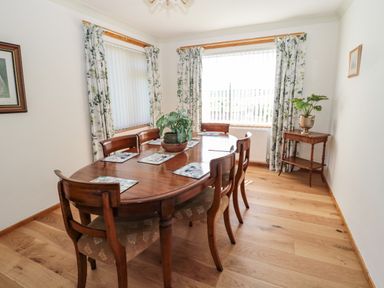 A dining room with a wooden table and six chairs next to windows with floral curtains at Rose Bank in Belford
