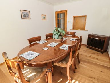 A dining room with a wooden table and six chairs a plant on the table and two framed pictures on the wall at Rose Bank in Belford