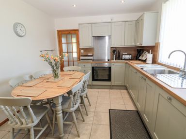A kitchen with a dining table and chairs next to countertops and cabinets at Rose Bank in Belford