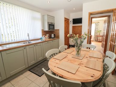 A kitchen with a wooden dining table and six chairs with placemats and flowers on the table at Rose Bank in Belford