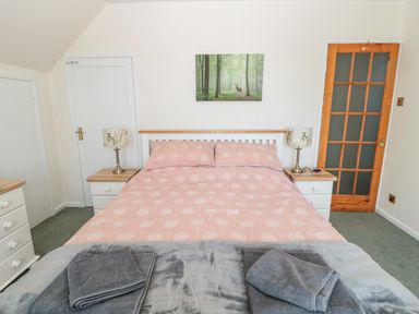 A bedroom with a double bed pink bedding two bedside tables with lamps and folded towels at Rose Bank in Belford