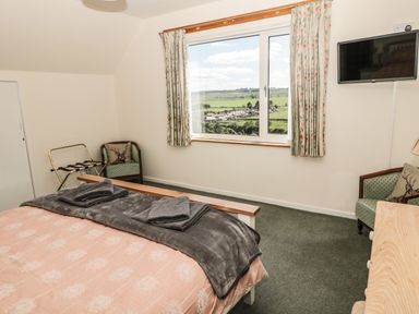 A bedroom with a bed and folded towels a window with curtains a television on the wall and two chairs at Rose Bank in Belford