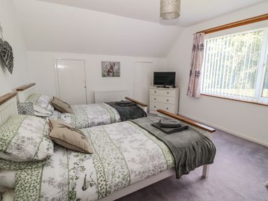 A bedroom with two single beds a chest of drawers with a television and a large window at Rose Bank in Belford