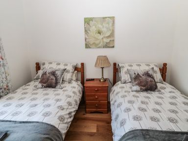 A bedroom with two single beds a nightstand with a lamp and a remote and floral artwork on the wall at Rose Bank in Belford