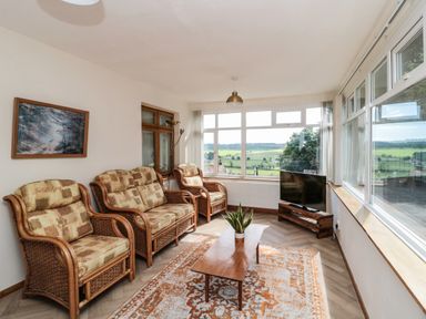 A sitting room with wicker furniture and a coffee table in front of large windows showing a rural view at Rose Bank in Belford