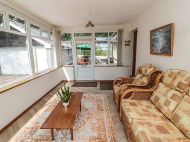 A sunroom with wicker sofas a wooden coffee table with a plant and large windows at Rose Bank in Belford