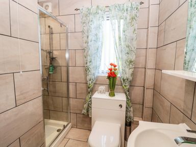 A bathroom with a glass shower cubicle a white toilet a sink and a window with floral curtains at Rose Bank in Belford
