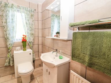 A bathroom with a toilet, a sink with a cabinet, a mirror cabinet, green towels on a rack, and a window with floral curtains at Rose Bank in Belford