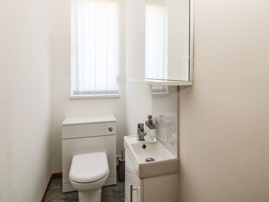 A small bathroom with a toilet, a sink with a cabinet, a mirror, and a window with vertical blinds at Rose Bank in Belford