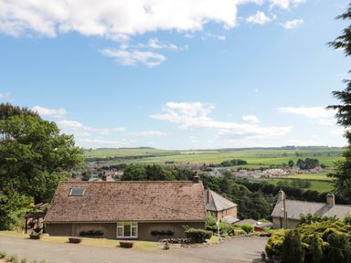 A house with a tiled roof and flower boxes on the wall surrounded by trees with fields and other houses in the background at Rose Bank in Belford