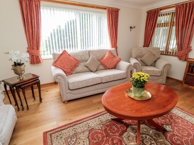 A living room with beige sofa and armchair orange cushions wooden side tables and round coffee table with a plant on a patterned rug at Rose Bank in Belford