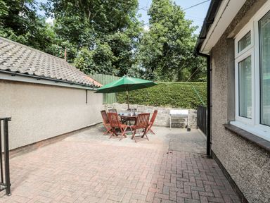 An outdoor patio with a round table and chairs under a green umbrella and a barbecue grill at Rose Bank in Belford
