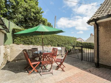 An outdoor patio with wooden chairs and a table under a green umbrella at Rose Bank in Belford