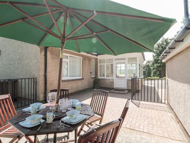 A patio area with a wooden dining table and chairs under a green umbrella at Rose Bank in Belford