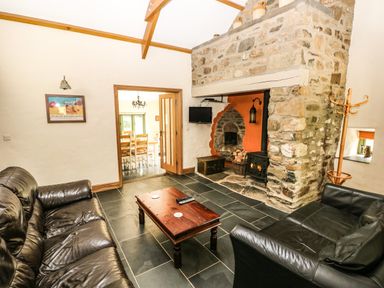 A living room with two black leather sofas a wooden coffee table and a stone fireplace with a wood burner at Trewrach Cottage in Dinas Cross