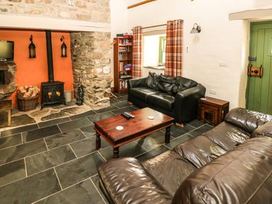 A living room with leather sofas a wood burning stove and a wooden coffee table at Trewrach Cottage Dinas Cross
