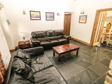 A living room with two leather sofas a wooden coffee table a side table with a lamp and three framed pictures on the wall at Trewrach Cottage in Dinas Cross