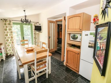 A kitchen dining area with a wooden table and chairs near green framed glass doors at Trewrach Cottage in Dinas Cross
