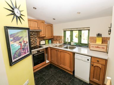 A kitchen with wooden cabinets a dishwasher an oven and a sink under a window at Trewrach Cottage in Dinas Cross
