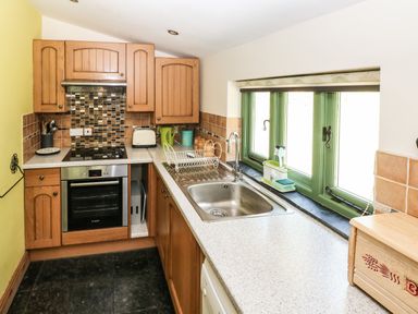 A kitchen with wooden cabinets a sink oven stovetop and green window frames at Trewrach Cottage in Dinas Cross