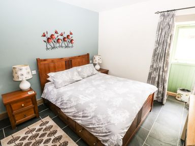 A bedroom with a wooden bed and bedside tables with lamps and a green door at Trewrach Cottage in Dinas Cross