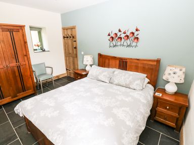 A bedroom with a double bed two bedside tables lamps a wooden wardrobe a chair and a door at Trewrach Cottage in Dinas Cross
