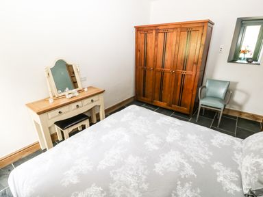 A bedroom with a wooden wardrobe vanity table chair and bed at Trewrach Cottage in Dinas Cross