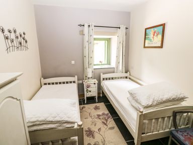 A bedroom with two single beds a small decorated nightstand a window with curtains and a framed picture on the wall at Trewrach Cottage in Dinas Cross