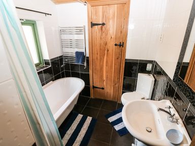A bathroom with a bathtub sink toilet rugs wooden door and towel rail at Trewrach Cottage in Dinas Cross