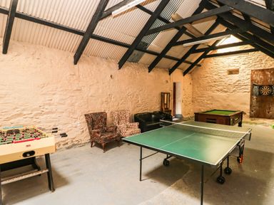 A game room with a foosball table ping pong table armchairs and a pool table at Trewrach Cottage in Dinas Cross