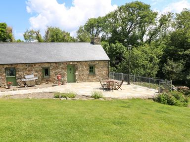 Stone cottage with green doors and windows and a patio with table and chairs and a grill in a garden at Trewrach Cottage in Dinas Cross