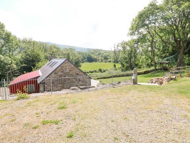 A stone house with a red extension near a fenced garden and green fields at Trewrach Cottage in Dinas Cross