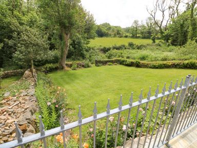 A garden with a metal fence stone walls flowers trees and grass at Trewrach Cottage in Dinas Cross