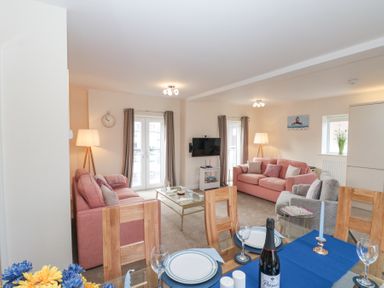 A living room with two pink sofas a grey armchair a glass coffee table and a dining table with plates and a bottle of prosecco at Weydale Avenue in Scarborough