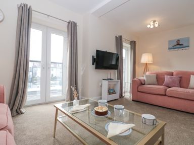 A living room with pink sofas a glass coffee table a wall mounted television and french doors at Weydale Avenue in Scarborough