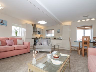 An open plan living room and kitchen with pink sofas a grey armchair a glass coffee table with cups and cake and a wooden dining table with chairs at Weydale Avenue in Scarborough