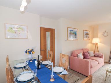 A dining area with a glass table set with plates and glasses next to a living area with a pink sofa and a standing lamp at Weydale Avenue in Scarborough