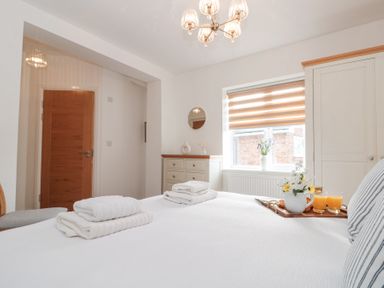 A bedroom with white bed linens folded towels a wooden door a window with blinds and a small chest of drawers at Weydale Avenue in Scarborough