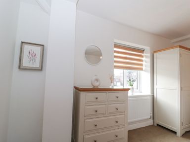 A bedroom corner with a chest of drawers, a wardrobe, a window with blinds, a wall mirror, and a framed picture on the wall at Weydale Avenue Scarborough