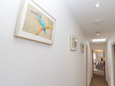 A hallway with framed bird pictures on the wall and a view into a living room and kitchen at Weydale Avenue in Scarborough