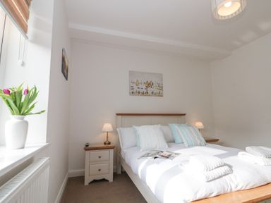 A bedroom with a bed with pillows and folded towels a nightstand with a lamp and a vase with flowers on the windowsill at Weydale Avenue in Scarborough