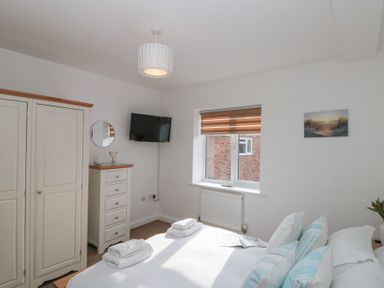 A bedroom with a bed towels and pillows a wardrobe chest of drawers a wall mounted tv and a window with blinds at Weydale Avenue Scarborough